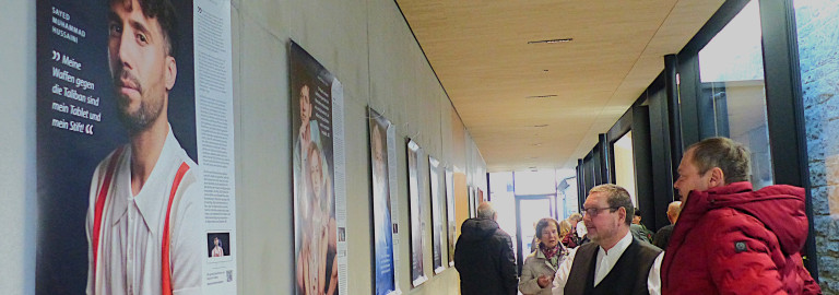 Zwei Personen betrachten ein großes Ausstellungsplakat mit dem Portraitfoto eines Mannes.