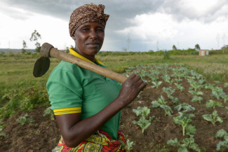 Flora Ryoba, Dorfbewohnerin in Kewamba/Tansania steht mit ihrer Hacke vor dem Gemüsefeld der örtlichen Frauengruppe