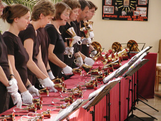 Handglockenspielerinnen stehen hinter einem langen Tisch mit den Instrumenten.